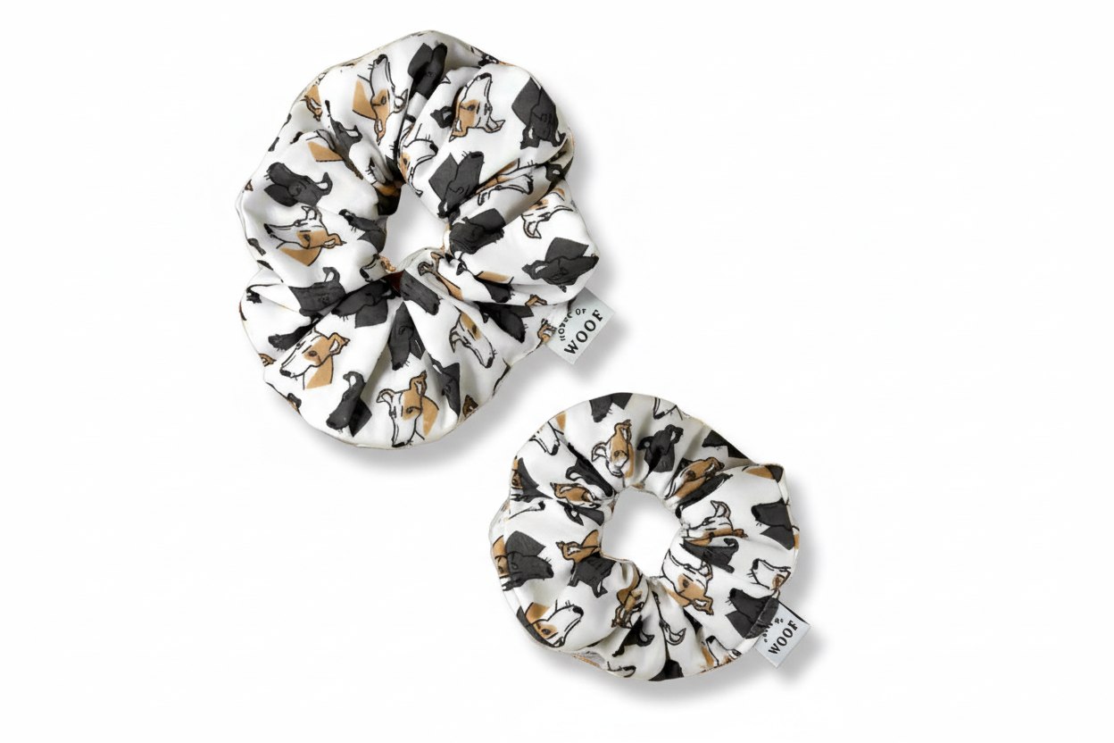 Pair of white fabric hair scrunchies with a hand-drawn Greyhound print in tan, black, and white, designed by House of Woof.