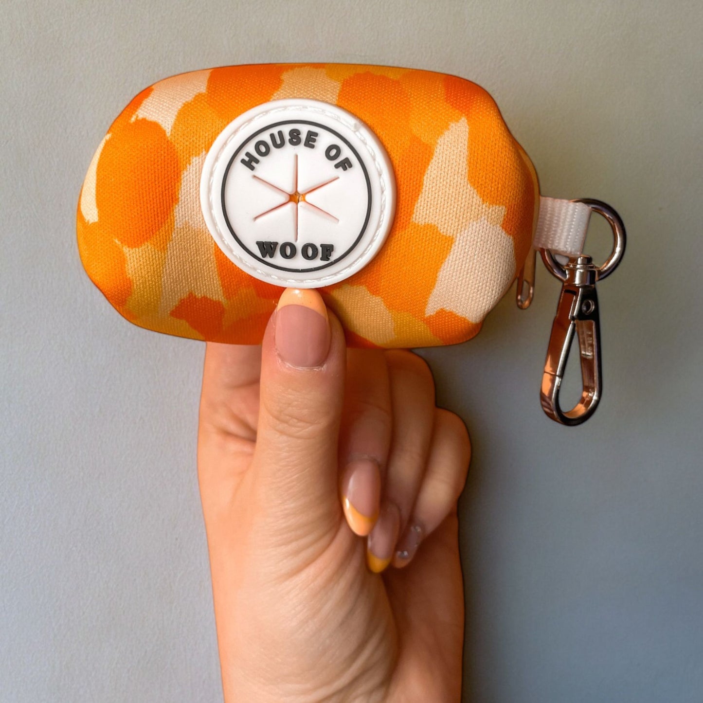 Orange and yellow dog poo bag holder from House of Woof held in a hand against a grey background