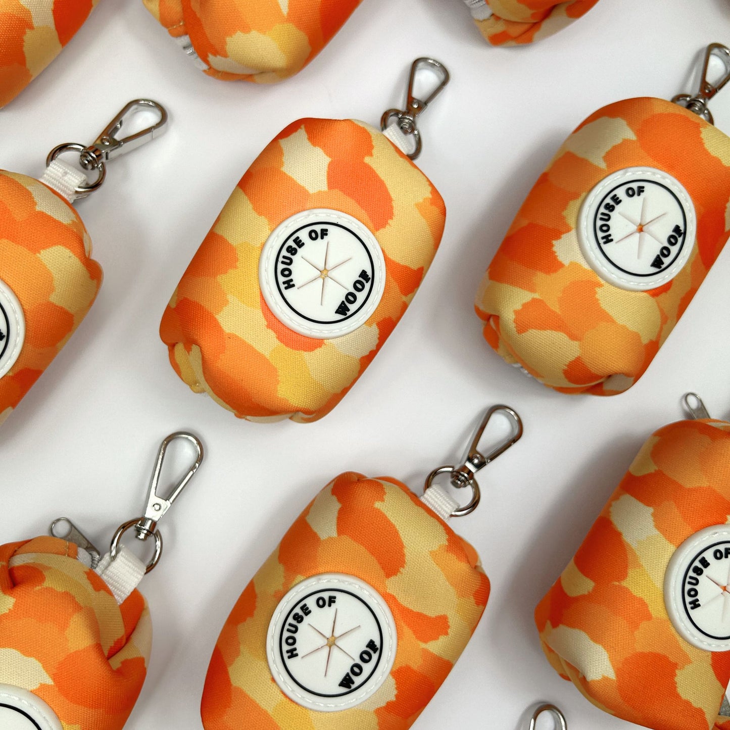 Multiple orange and yellow dog poo bag holders from House of Woof displayed on a white background