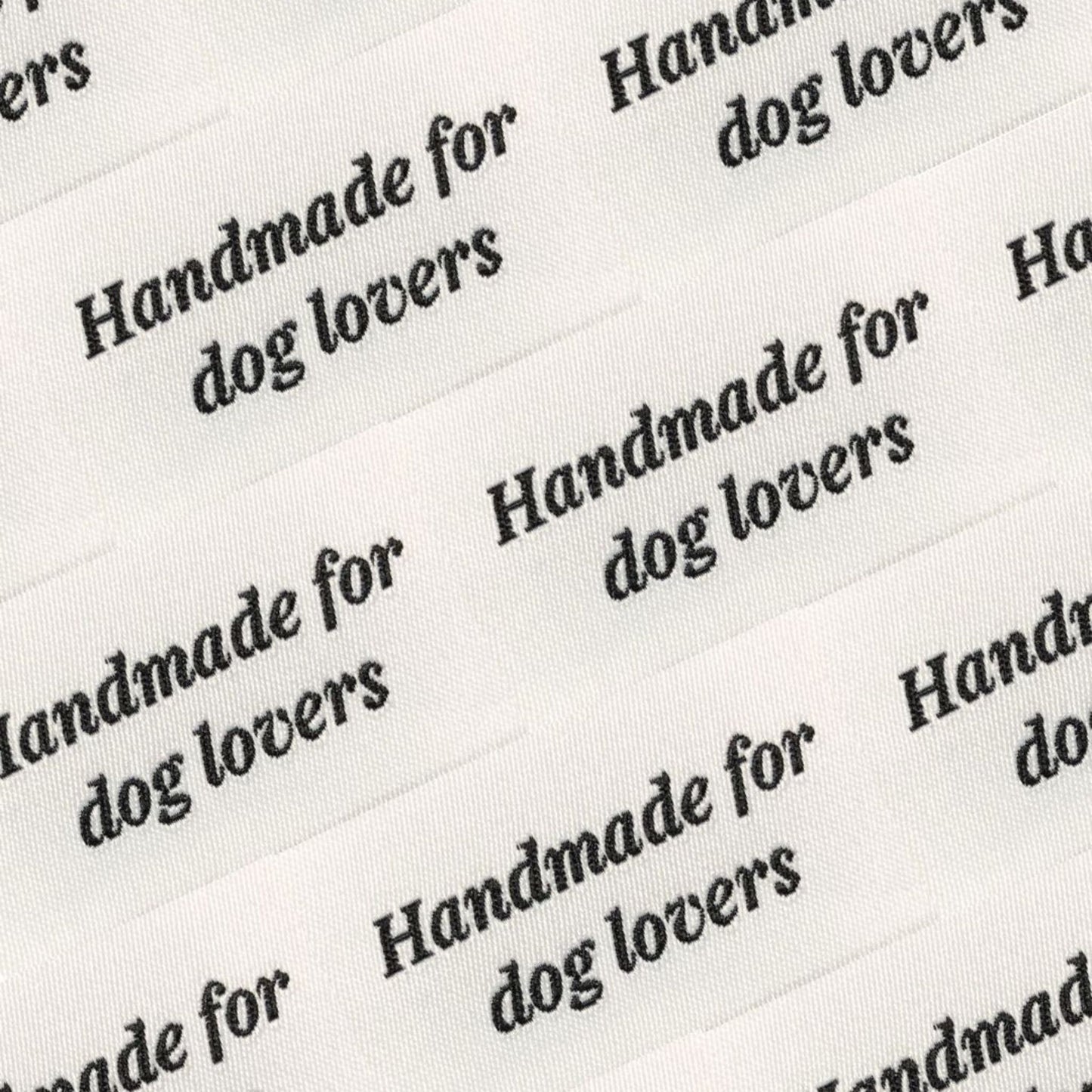 Close-up of white fabric labels with black text reading “Handmade for dog lovers,” used for House of Woof handmade pet accessories.