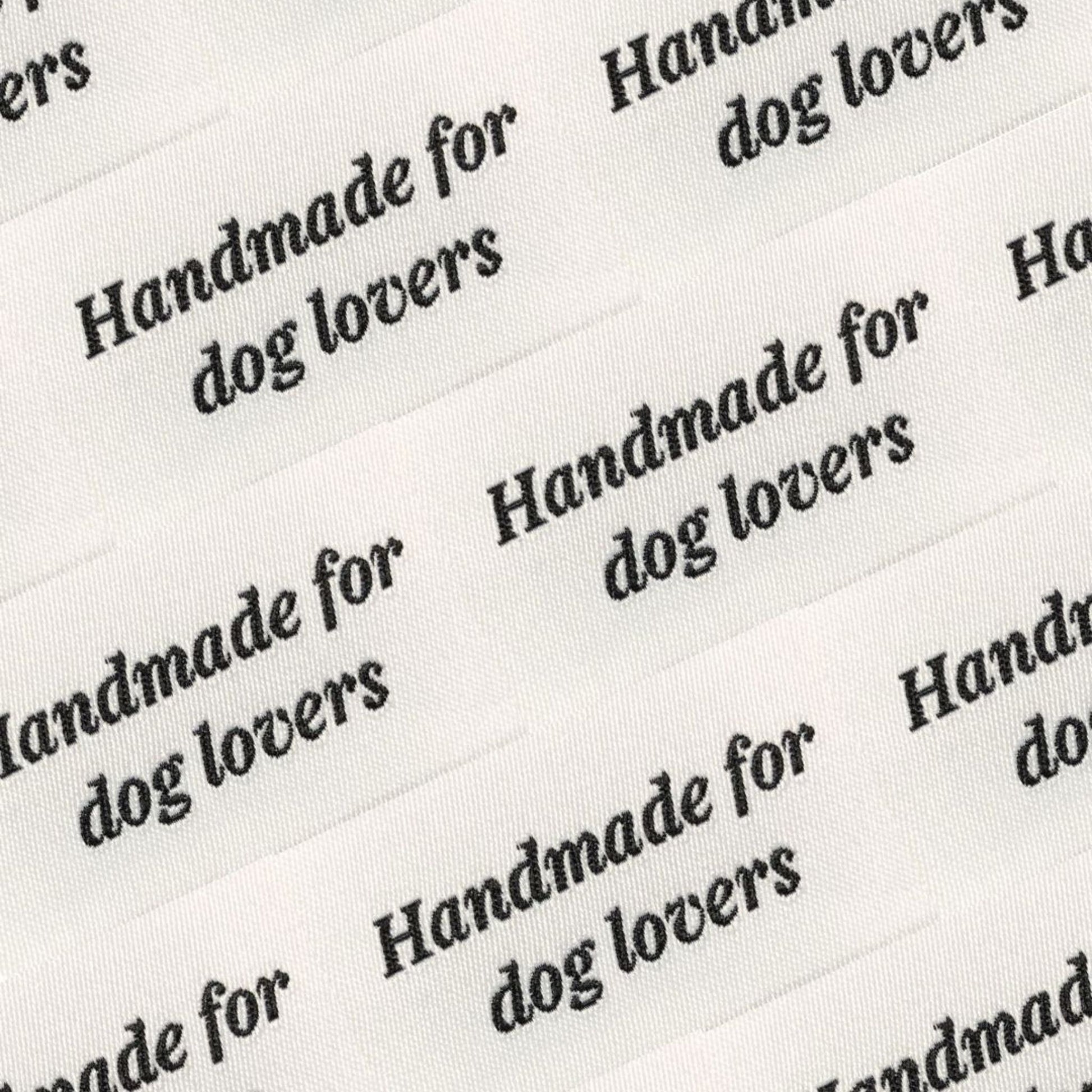 Close-up of white fabric labels with black text reading “Handmade for dog lovers,” used for House of Woof handmade pet accessories.